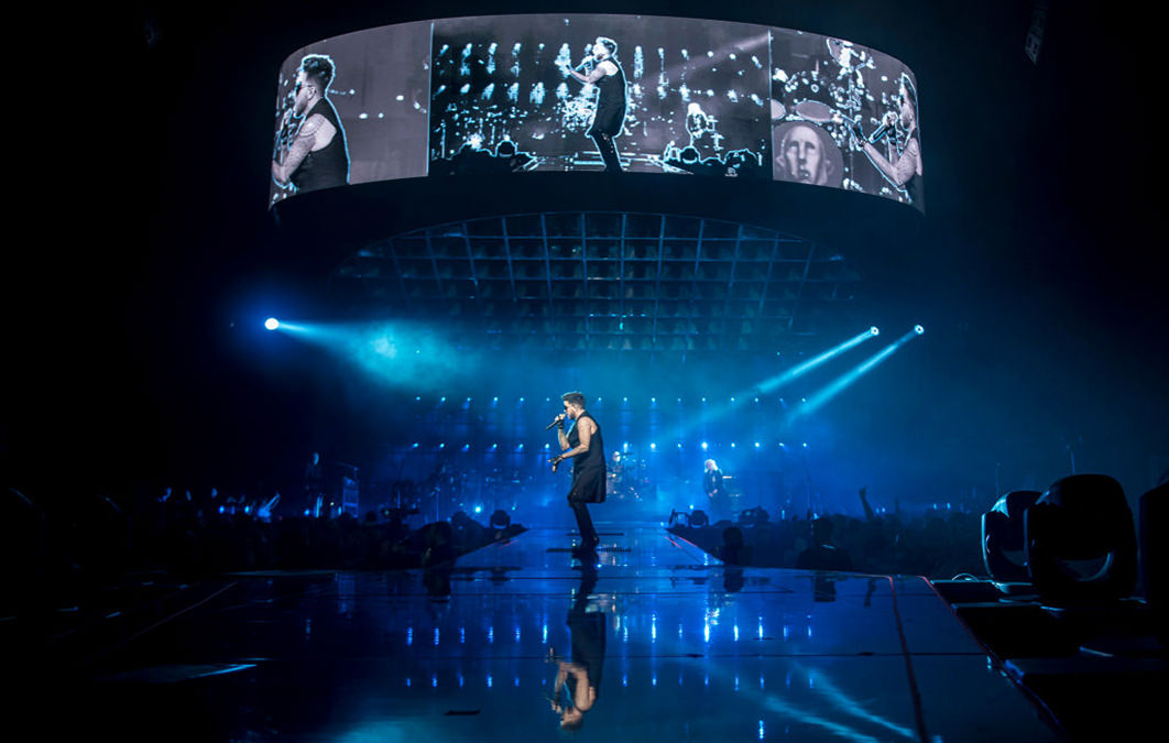 Adam Lambert playing with Queen on blue lit stage