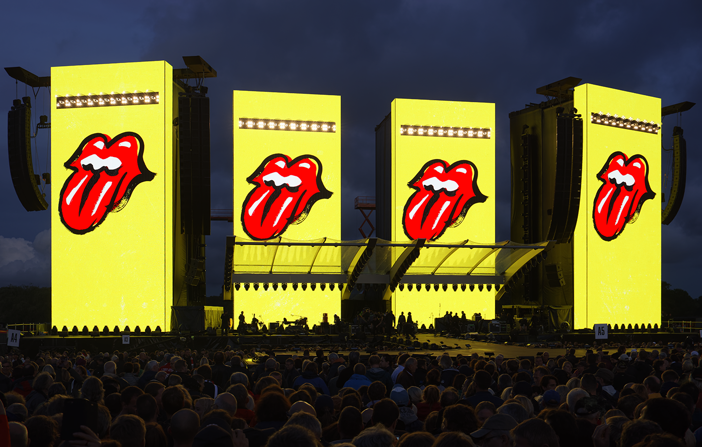 Four portrait mode video displays show the Rolling Stone tongue logo on yellow backgrounds