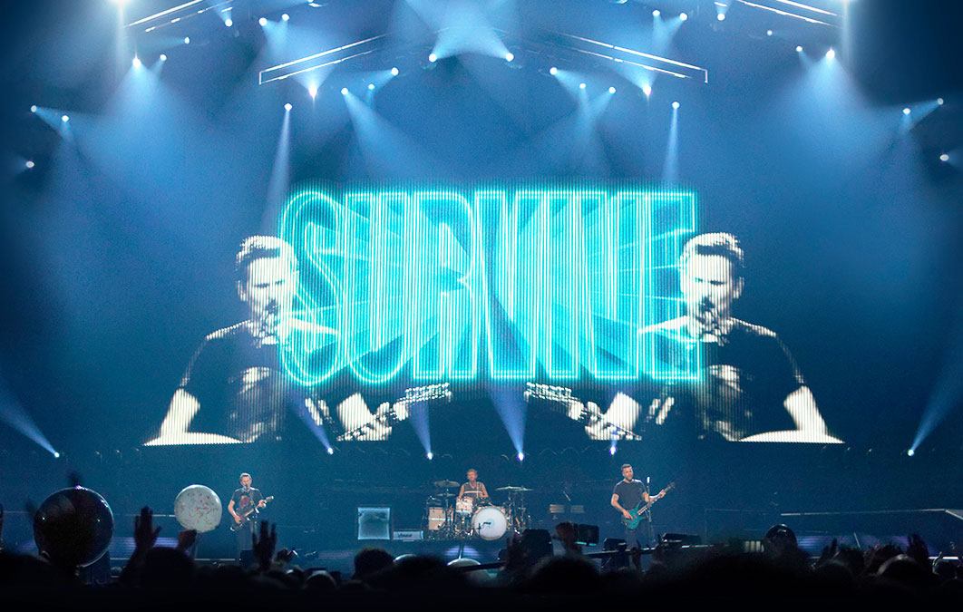 matt bellamy of muse seen on LED screen with survive written across his face