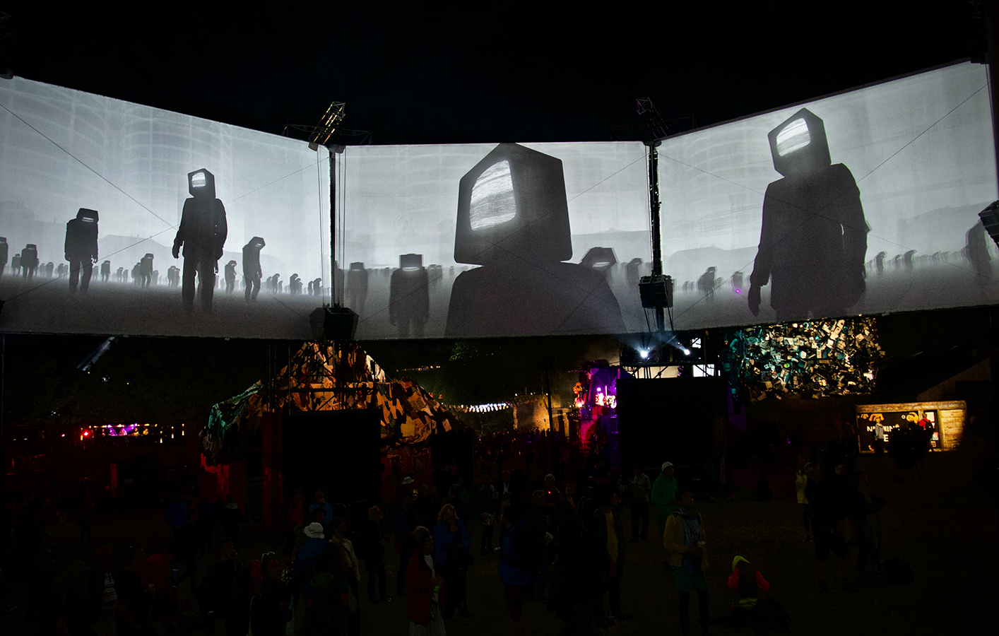 Science fiction style design of people with computer screens for heads displayed across three LED screens