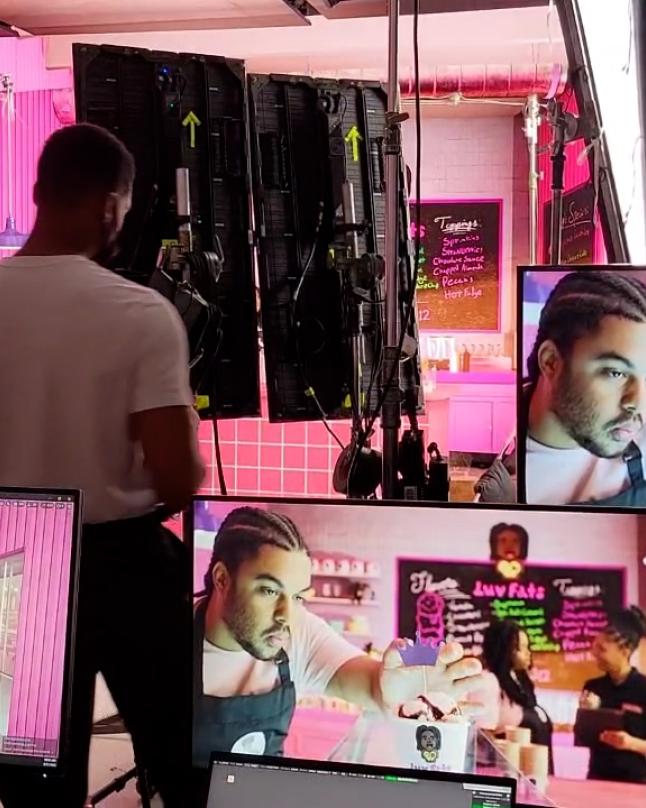 Production crew monitors a commercial shoot inside a virtual production stage, with multiple screens displaying a brightly lit, pink-themed scene featuring a performer interacting on camera.
