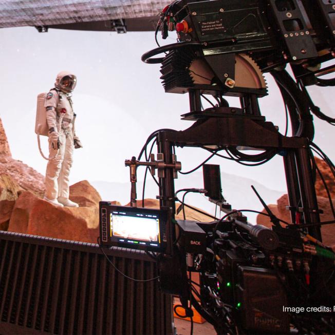 Camera films man in space suit on stage