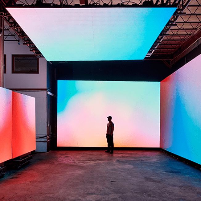 Man stands between multiple LED screen with colourful print