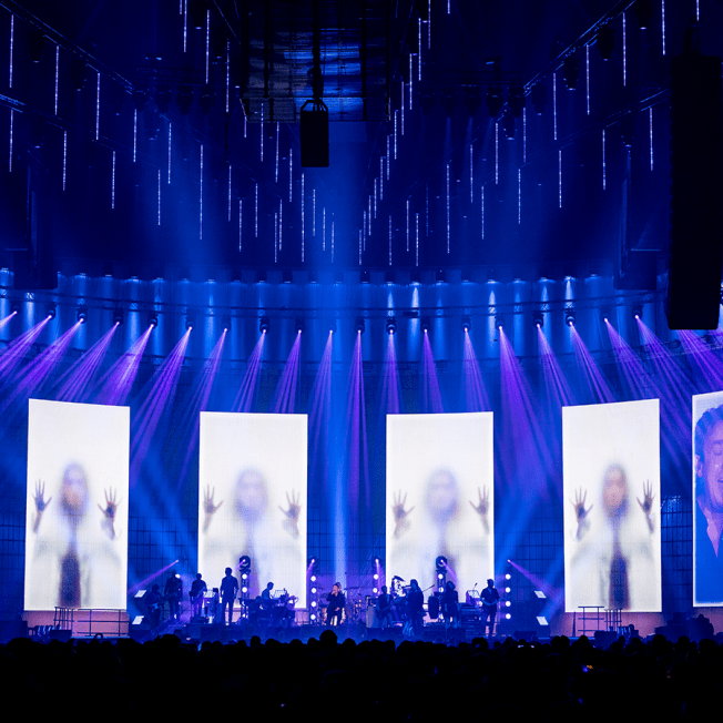 Band playing in front of screens with video of women behind frosted glass