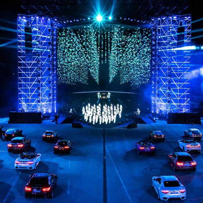 Several maserati cars parked in front stage with multiple dancers performing