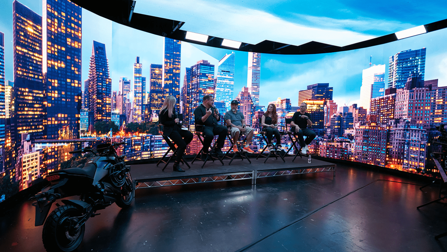 Panel with four 5 speakers in front of LED screen displaying city landscape
