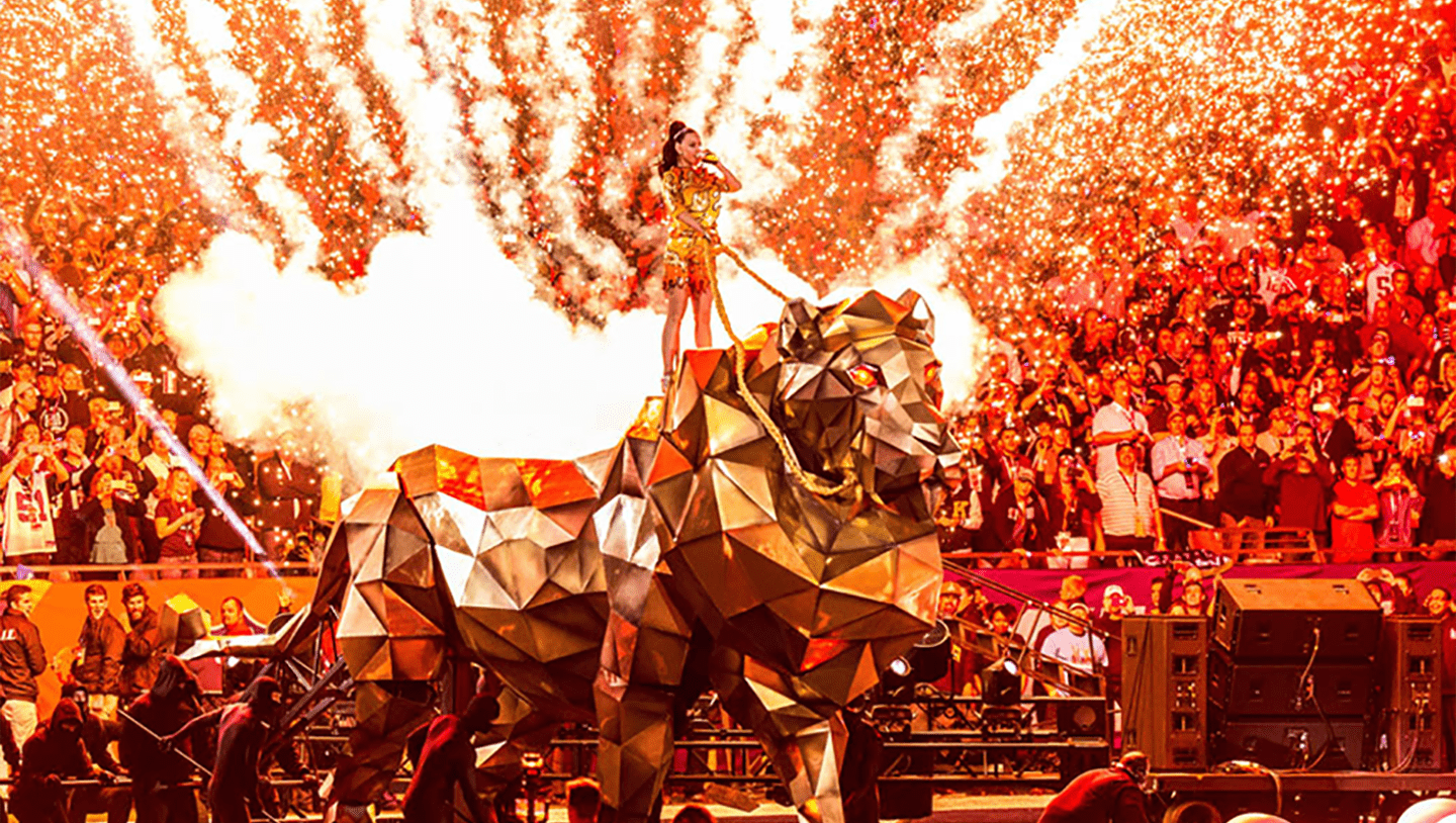 Katy Perry singing while standing on large mettalic lion