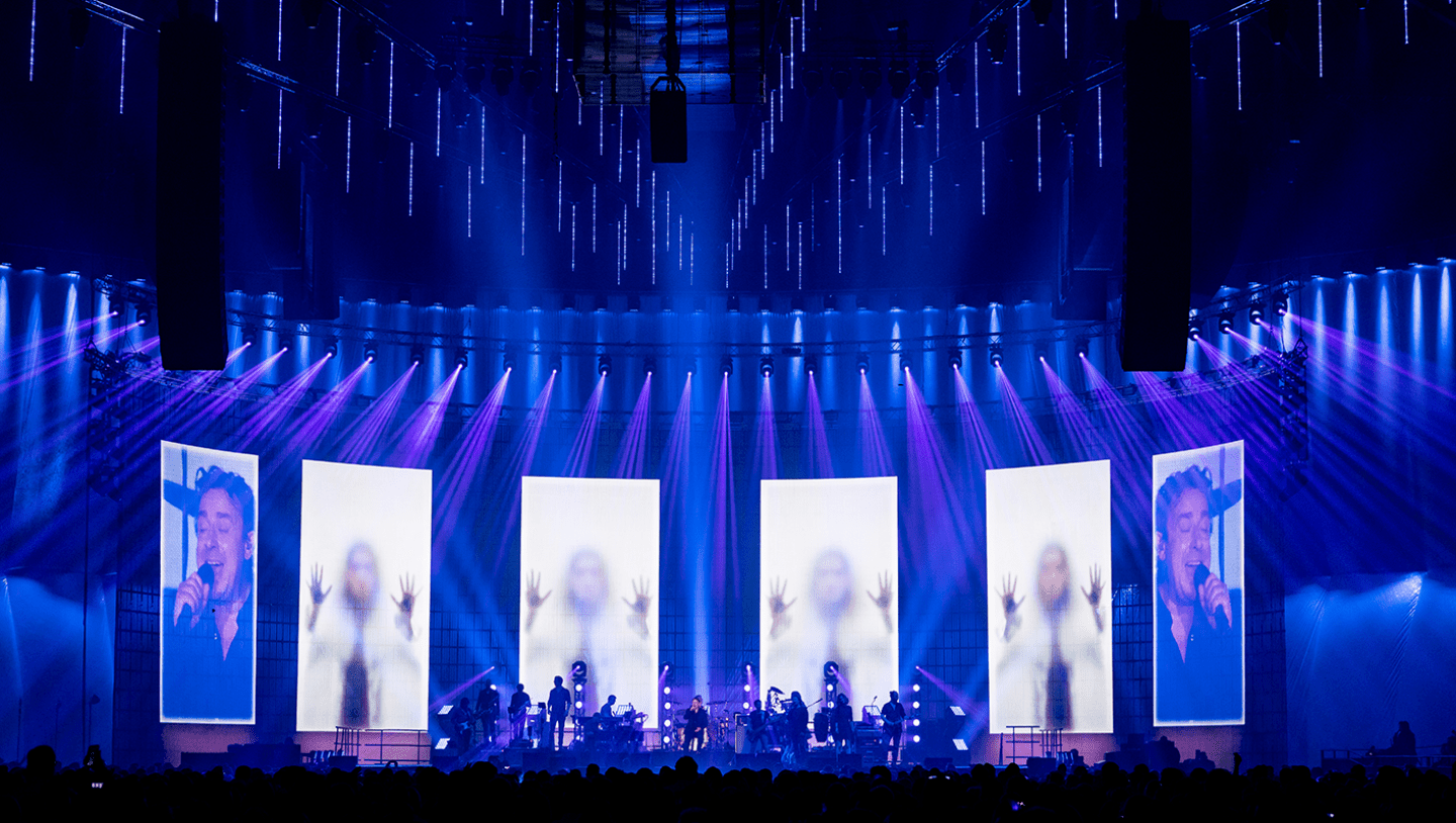 Band playing in front of screens with video of women behind frosted glass