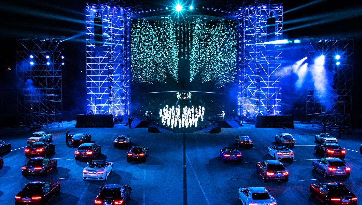 Several maserati cars parked in front stage with multiple dancers performing