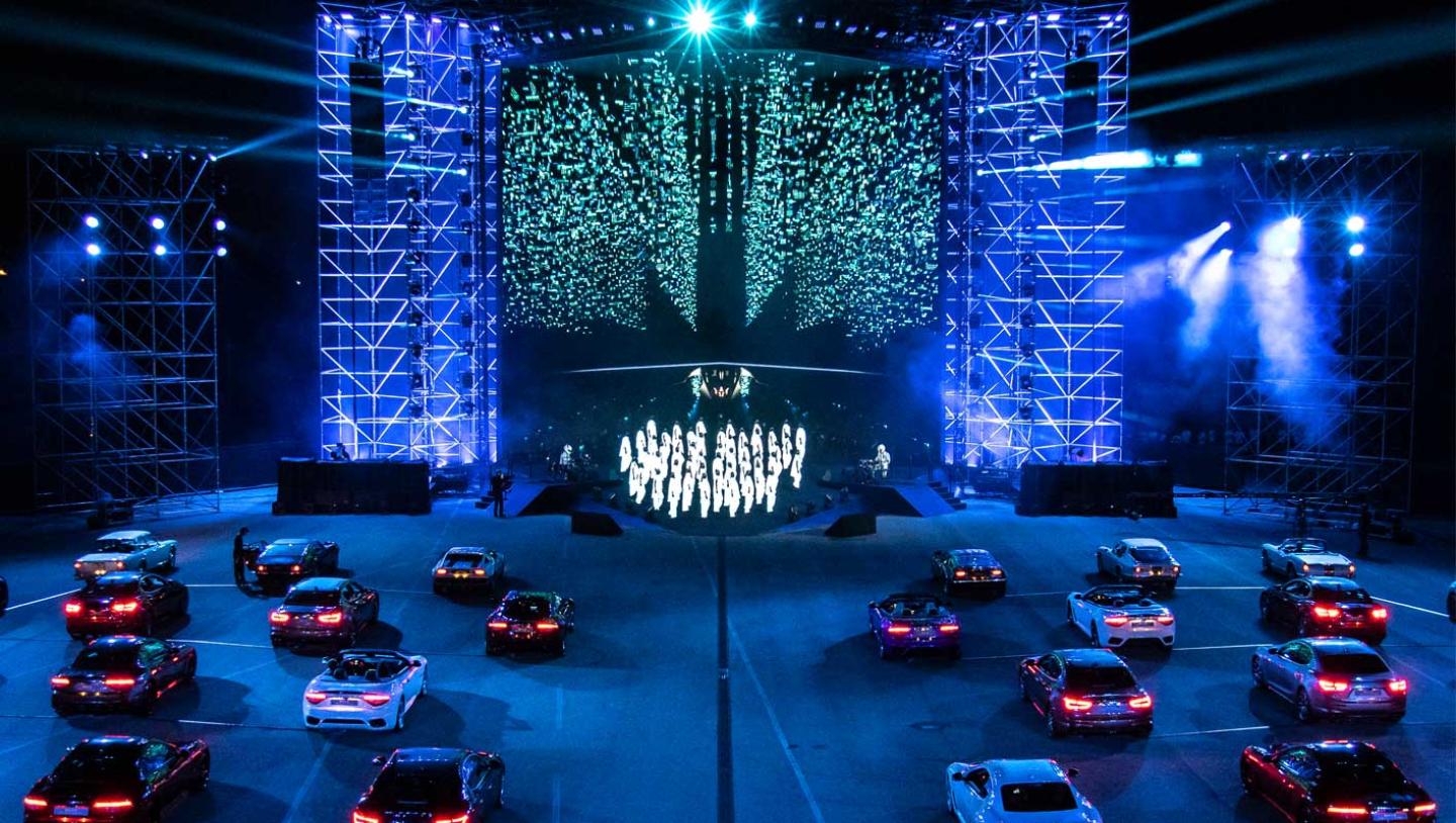 Several maserati cars parked in front stage with multiple dancers performing