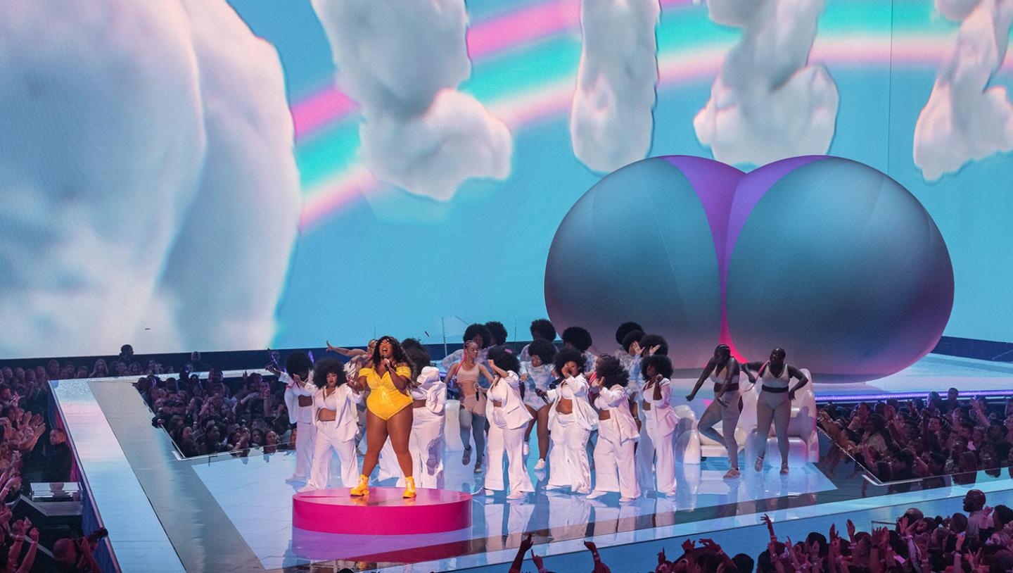 Lizzo playing on stage with large group of singers 