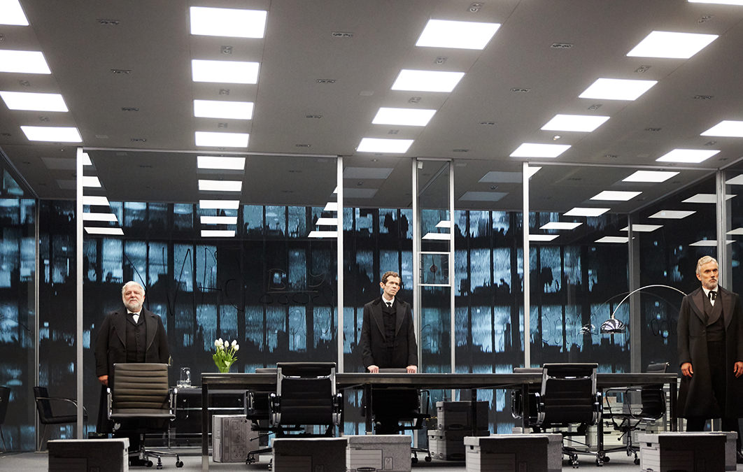 Actors on stage in office environment during performance of The Lehman Trilogy