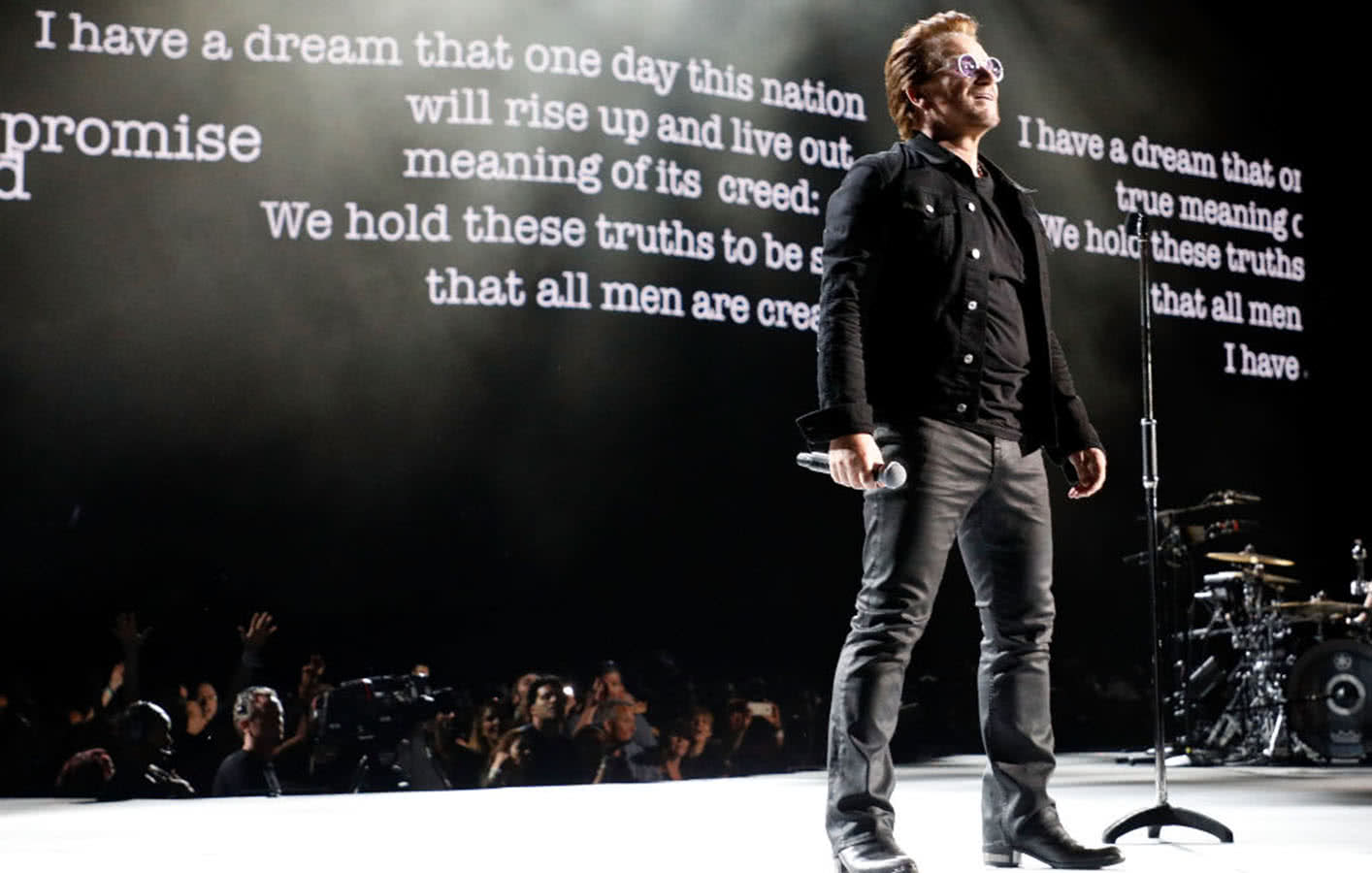 Bono on stage with quotes from Martin Luther King displaying on video display