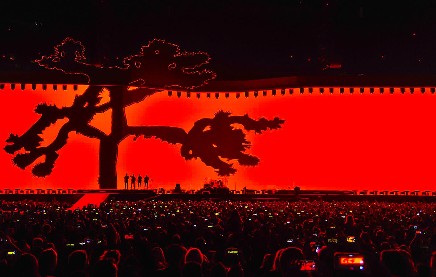 u2 standing on stage in front of red video screen featuring Joshua Tree iconography